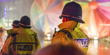 Police officers in high-visibility jackets watching over a vibrant event with colourful parachute-like decorations in the background.