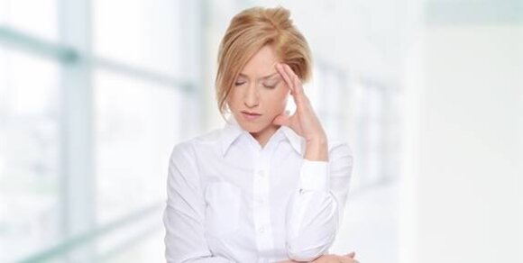A woman in a white shirt appears distressed, resting her forehead on her hand in a bright, uncluttered environment.