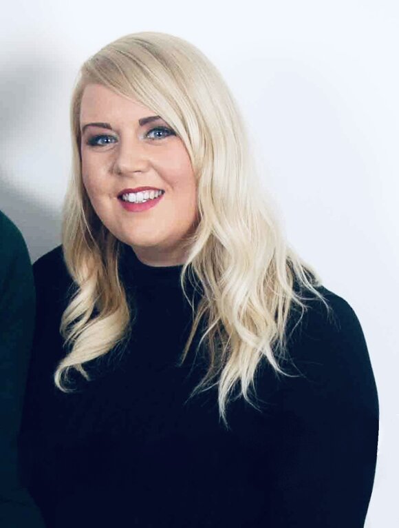 A smiling woman with long blonde hair wearing a black top, against a plain background.