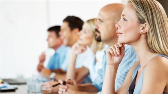 A group of five individuals attentively listening during a presentation, with focused expressions and hand gestures.
