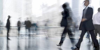 Blurred silhouettes of people walking in a modern urban setting, suggesting a busy environment.