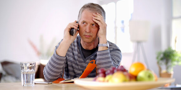 A concerned man on the phone, looking worried while sitting at a table with a bowl of fruit and a glass of water.