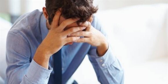 A man in a blue shirt sits with his head in his hands, conveying a sense of distress or frustration.